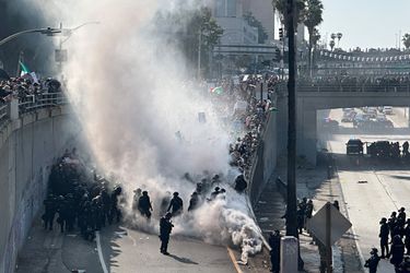 Police officers are enveloped in a cloud of smoke from tear gas and percussion grenades while guarding a highway onramp in Los Angeles